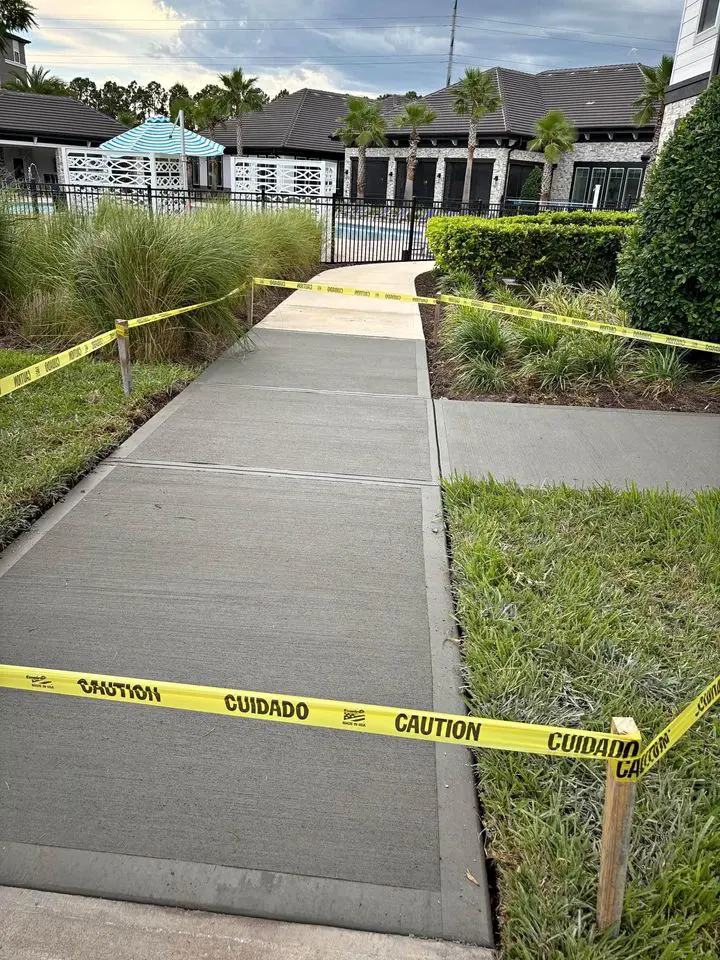 concrete sidewalk paved in fresh grey concrete, with a broom finish to make it non-slip. Yellow caution tape is around the area to prevent people walking in the fresh concrete