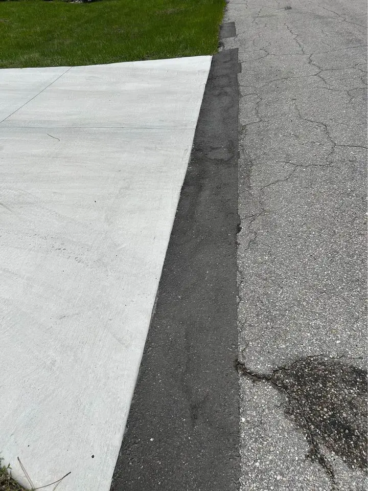 asphalt patch close up with hot mix asphalt freshly laid and compacted. Concrete driveway on the left of the image, new asphalt patch in the middle, old asphalt to the right