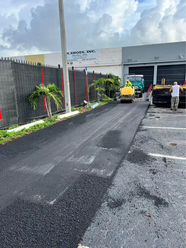 resurfacing a small parking lot in Boca Raton FL. Asphalt contractor in fluro vest driving a yellow roller, compacting black asphalt