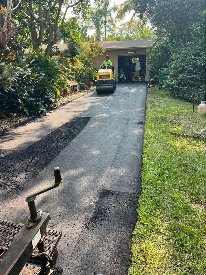 asphalt driveway that was removed is being repaved with fresh hot mix asphalt. contractor driving yellow compactor roller. picture taken from perspective of paving machine operator