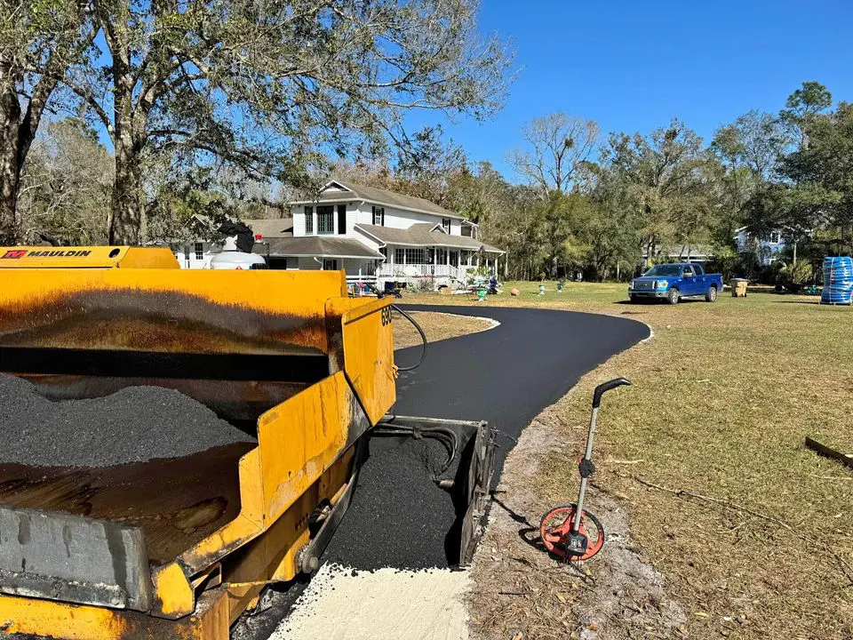 yellow asphalt paving machine in the foreground, with a freshly laid driveway at large florida home