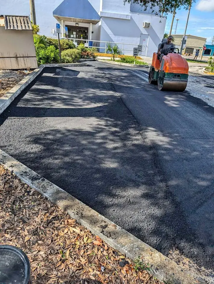 asphalt contractor on an asphalt steam roller compacting some asphalt hot mix that has been laid at a parking lot in boca raton fl